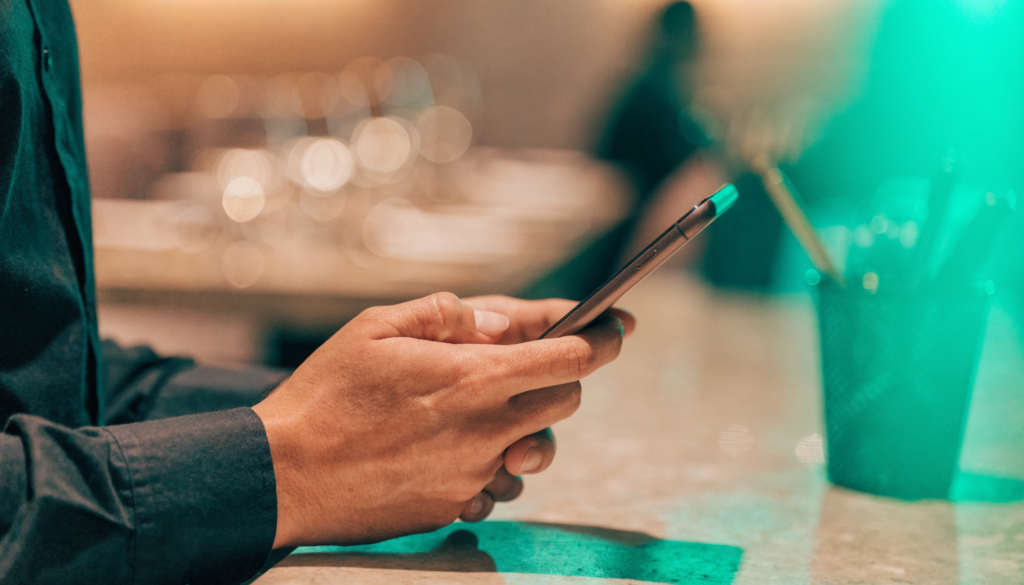 Mãos de anfitrião segurando smartphone em recepção de reservas de restaurante com mesa ao fundo