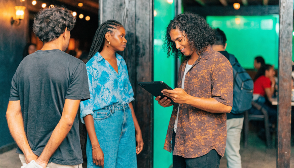 Anfitrião com tablet organizando pequena fila de clientes na entrada de restaurante à noite
