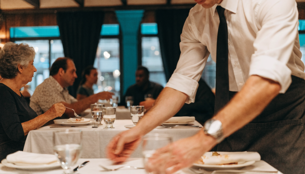 Garçom organizando e preparando uma mesa durante o serviço em restaurante movimentado