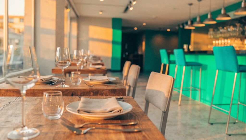 Interior aconchegante de restaurante ao entardecer com mesas de madeira postas e detalhes em turquesa